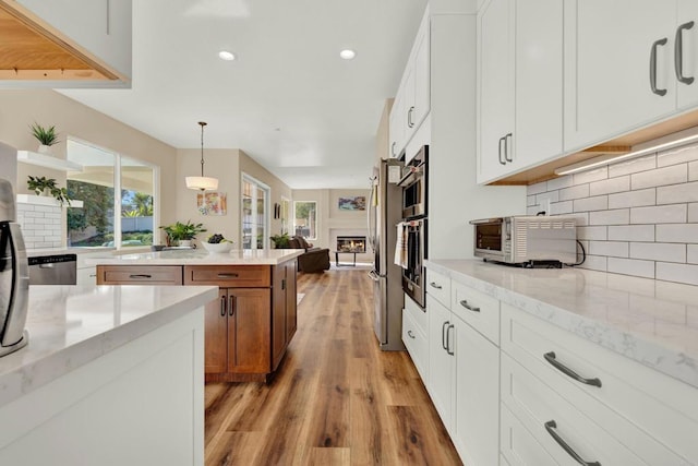 kitchen with hanging light fixtures, light stone countertops, white cabinets, and light wood-type flooring