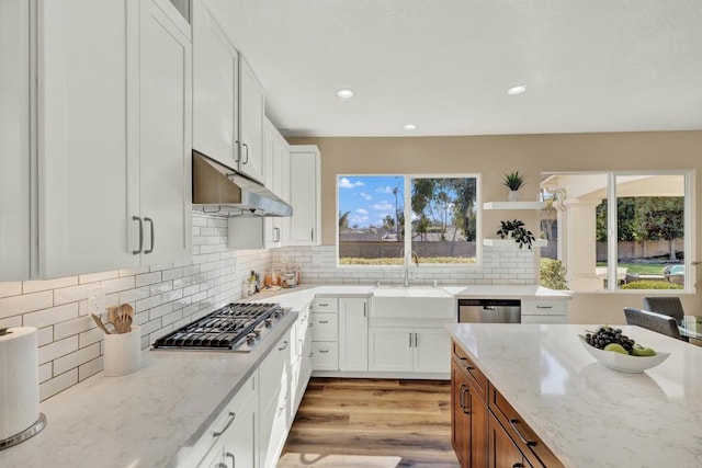 kitchen featuring appliances with stainless steel finishes, white cabinetry, sink, light stone countertops, and light hardwood / wood-style flooring