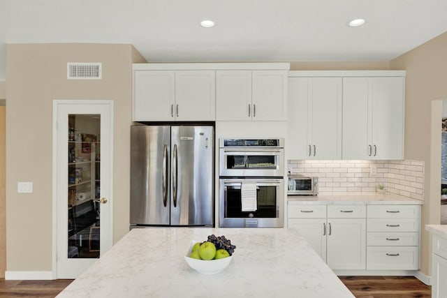 kitchen with light stone counters, tasteful backsplash, dark hardwood / wood-style floors, stainless steel appliances, and white cabinets