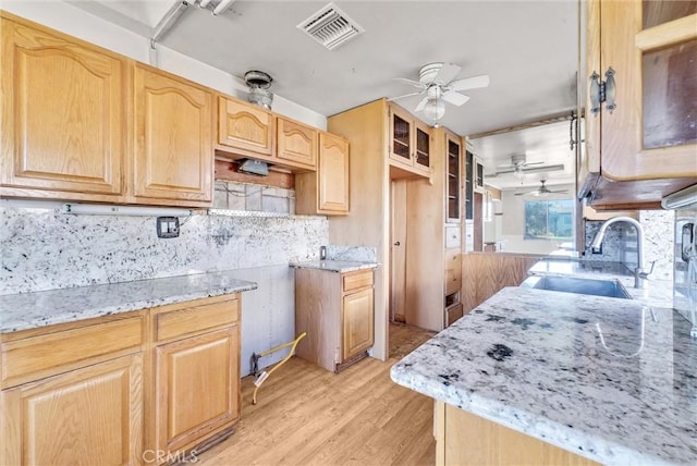 kitchen featuring sink, light hardwood / wood-style floors, backsplash, and light stone countertops