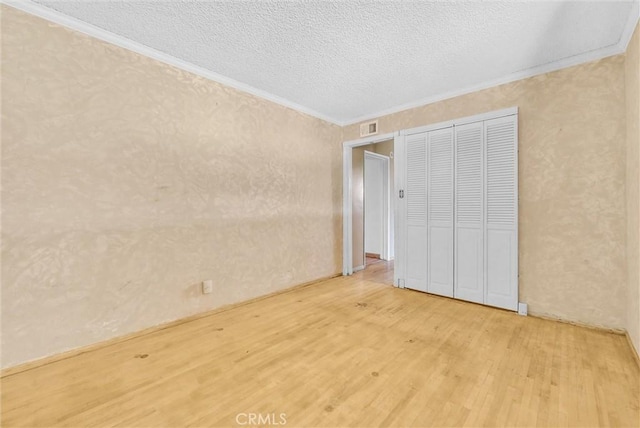 unfurnished bedroom with a textured ceiling, light hardwood / wood-style flooring, ornamental molding, and a closet