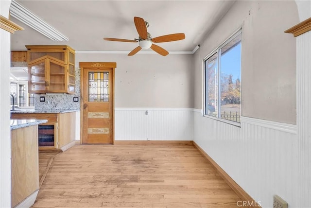 interior space with wine cooler, light hardwood / wood-style floors, ceiling fan, ornamental molding, and backsplash