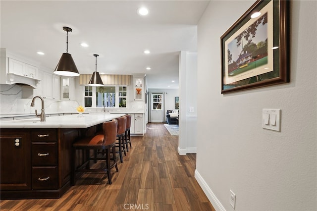 kitchen featuring a breakfast bar area, tasteful backsplash, decorative light fixtures, dark hardwood / wood-style flooring, and white cabinets