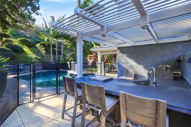 view of patio featuring an outdoor kitchen, a fenced in pool, a pergola, and a wet bar