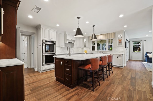 kitchen featuring a kitchen bar, white cabinetry, dark wood-type flooring, an island with sink, and double oven