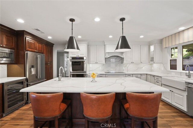 kitchen featuring white cabinets, a kitchen island with sink, stainless steel appliances, and wine cooler