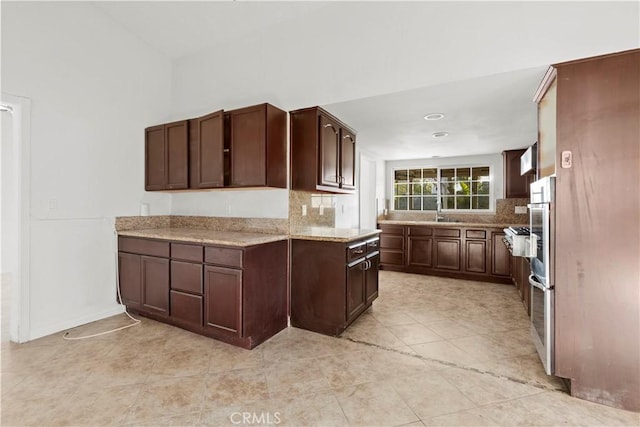 kitchen with decorative backsplash, light stone counters, dark brown cabinetry, and sink