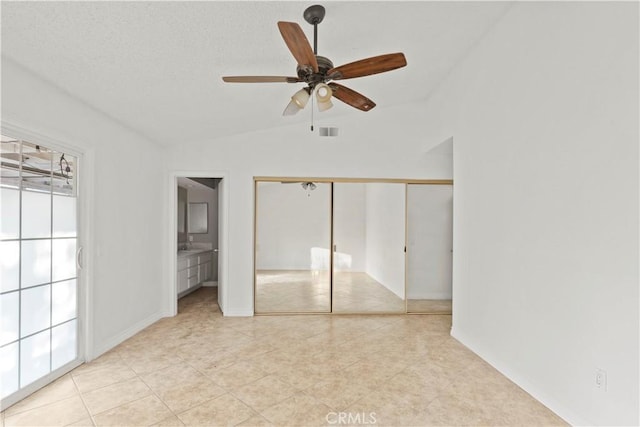 unfurnished bedroom featuring ceiling fan, lofted ceiling, light tile patterned flooring, connected bathroom, and a closet