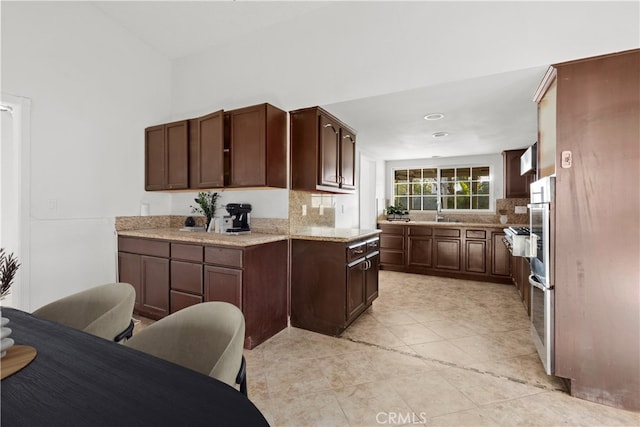 kitchen featuring decorative backsplash, sink, stainless steel oven, light tile patterned floors, and dark brown cabinets