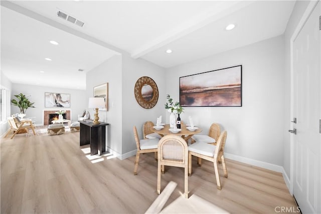 dining room featuring light wood-type flooring, a brick fireplace, and beamed ceiling