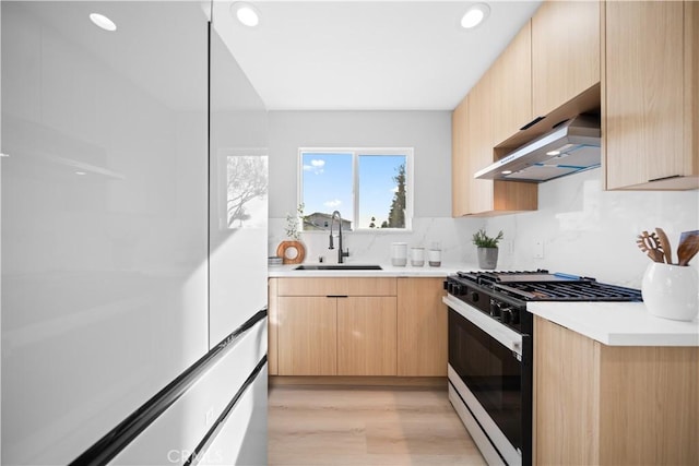 kitchen featuring light brown cabinetry, light wood-type flooring, backsplash, black gas range, and sink