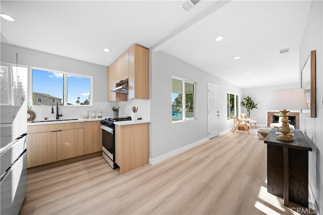 kitchen with sink, light hardwood / wood-style floors, decorative backsplash, range with gas stovetop, and light brown cabinets