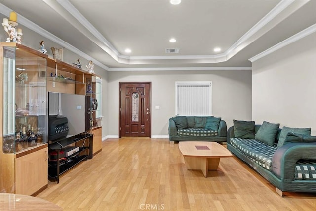 living room with light hardwood / wood-style floors, ornamental molding, and a tray ceiling