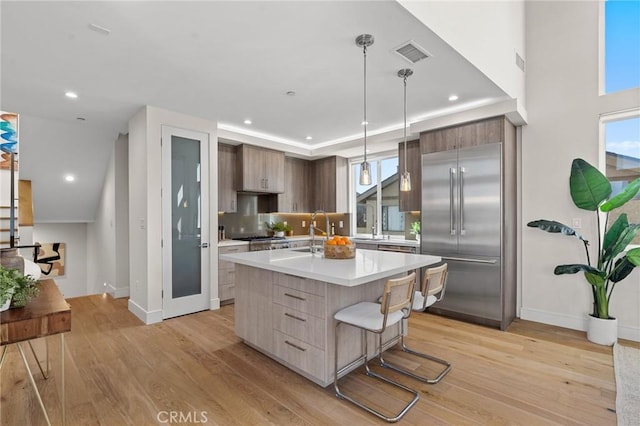 kitchen with appliances with stainless steel finishes, a kitchen breakfast bar, light wood-type flooring, and a center island with sink