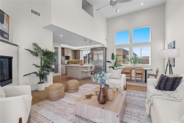 living room with a high ceiling, ceiling fan, and light hardwood / wood-style flooring