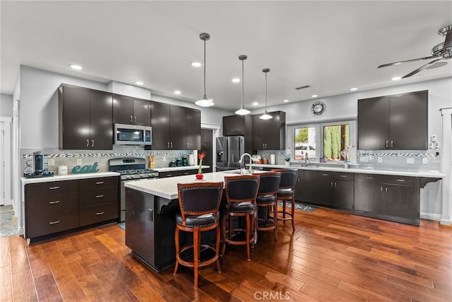 kitchen with a breakfast bar area, stainless steel appliances, light countertops, an island with sink, and pendant lighting