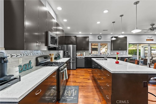 kitchen with stainless steel appliances, decorative light fixtures, a center island with sink, and a breakfast bar area