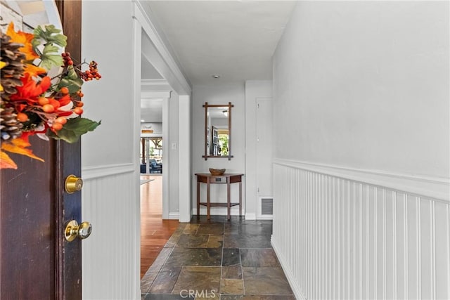 hallway featuring stone finish flooring, visible vents, and wainscoting