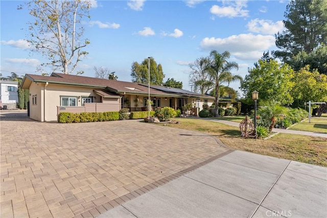 single story home with a front yard, roof mounted solar panels, and stucco siding