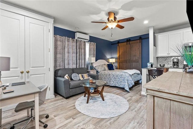 bedroom with light wood-style floors, a wall mounted air conditioner, and a barn door