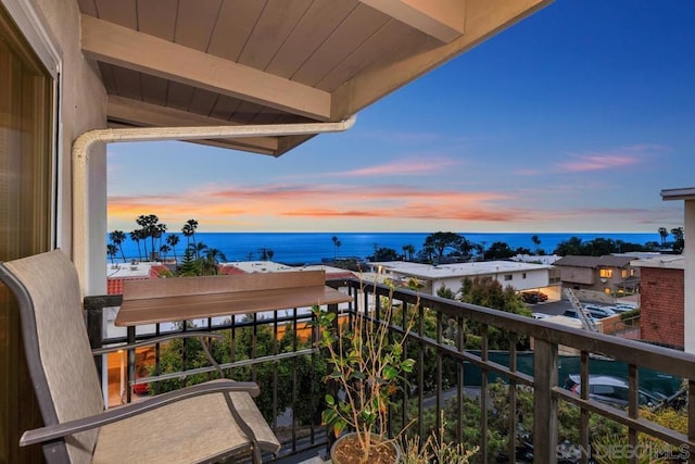 balcony at dusk featuring a water view