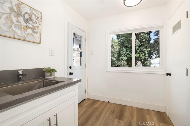 kitchen featuring sink, white cabinetry, dark stone countertops, and light hardwood / wood-style flooring