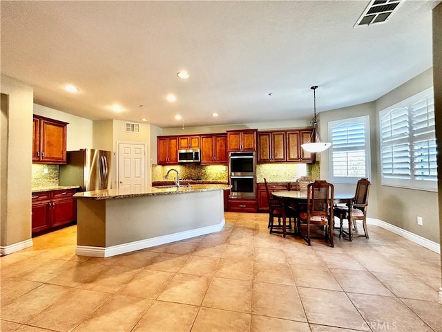 kitchen with a kitchen island with sink, backsplash, appliances with stainless steel finishes, decorative light fixtures, and light tile patterned flooring