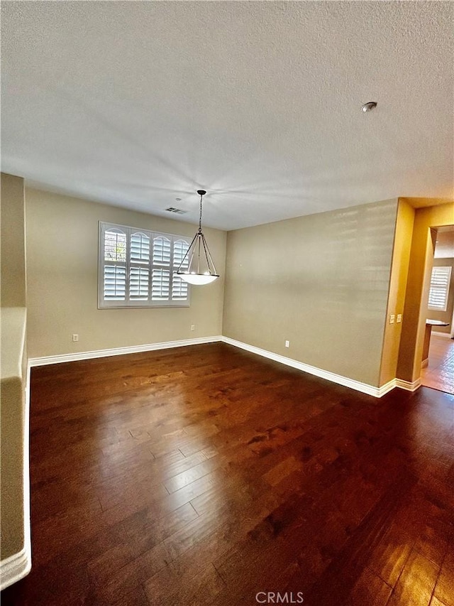 unfurnished room with dark wood-type flooring, a textured ceiling, and plenty of natural light