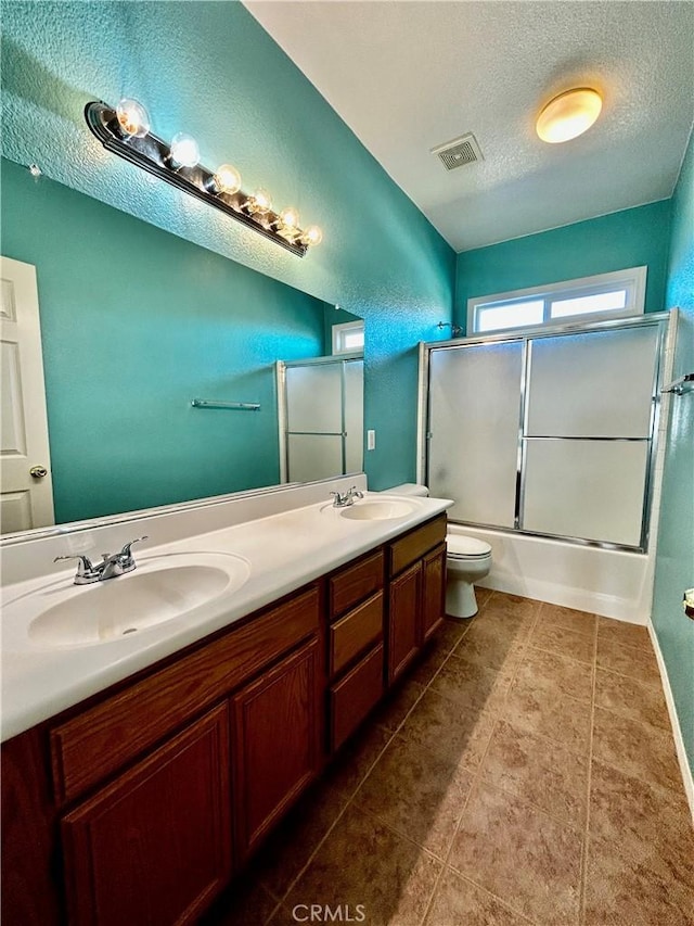 full bathroom featuring a textured ceiling, enclosed tub / shower combo, vanity, and toilet