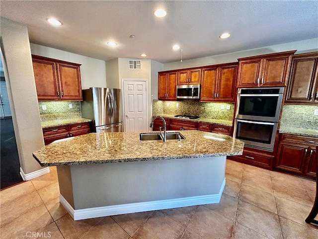 kitchen featuring sink, stainless steel appliances, an island with sink, and light stone counters