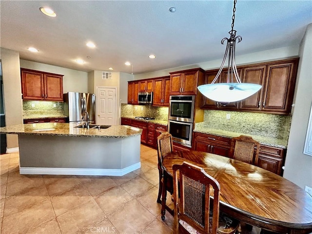 kitchen featuring sink, light stone counters, an island with sink, hanging light fixtures, and appliances with stainless steel finishes