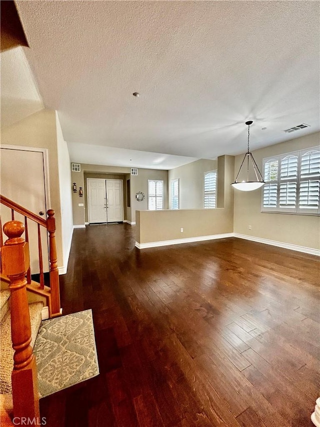 unfurnished living room with a textured ceiling, a wealth of natural light, and dark hardwood / wood-style floors