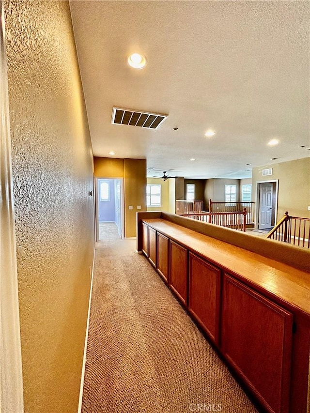 corridor with a textured ceiling and light colored carpet