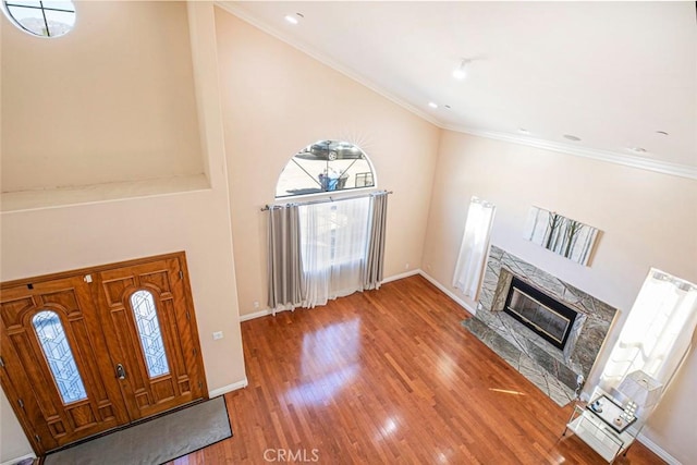 foyer featuring ornamental molding, wood-type flooring, a fireplace, and high vaulted ceiling