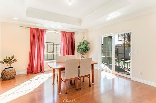 dining space featuring a tray ceiling, ornamental molding, and light wood-type flooring