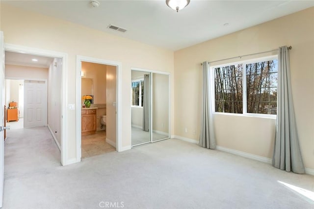 unfurnished bedroom featuring light carpet, ensuite bath, and a closet