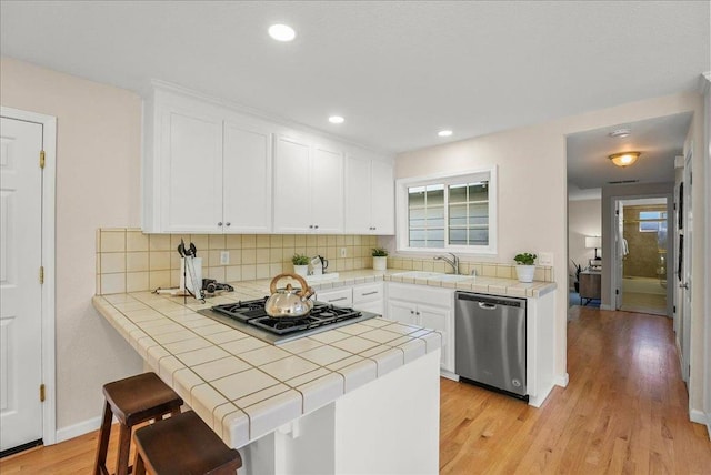 kitchen featuring appliances with stainless steel finishes, white cabinetry, kitchen peninsula, and tile counters