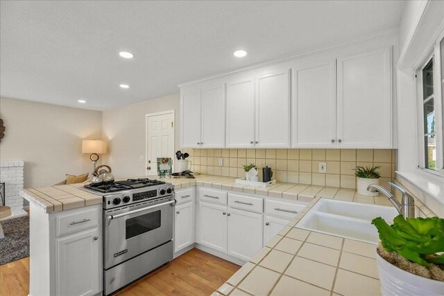 kitchen featuring kitchen peninsula, stainless steel gas range oven, tile countertops, white cabinets, and sink