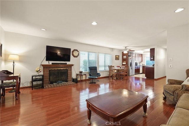 living room featuring a brick fireplace, hardwood / wood-style floors, and ceiling fan