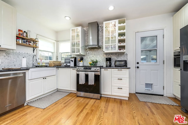 kitchen featuring white cabinets, light hardwood / wood-style flooring, backsplash, wall chimney range hood, and appliances with stainless steel finishes