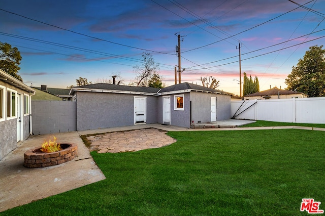 back house at dusk featuring a patio area, a yard, and a fire pit