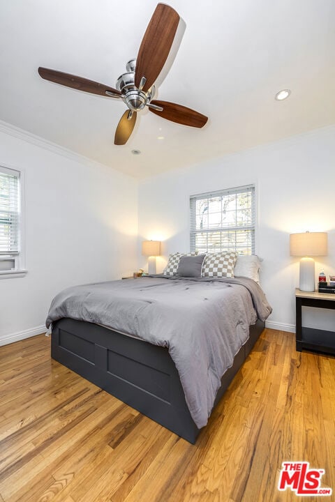 bedroom with ceiling fan, crown molding, light wood-type flooring, and multiple windows