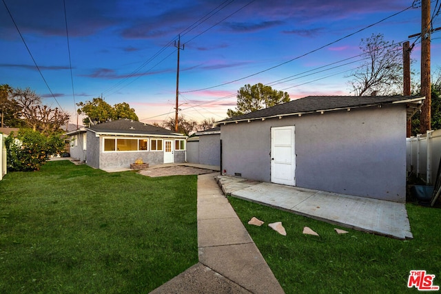 back house at dusk featuring a lawn and a patio