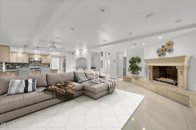 tiled living room with ceiling fan, sink, a fireplace, and beam ceiling