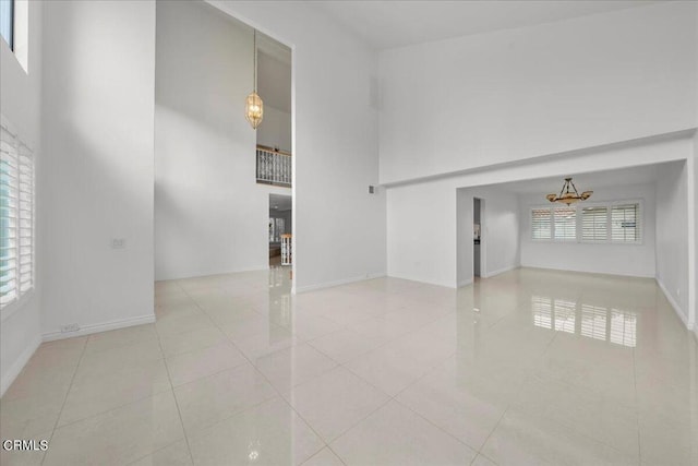 empty room with a high ceiling, a chandelier, and light tile patterned floors