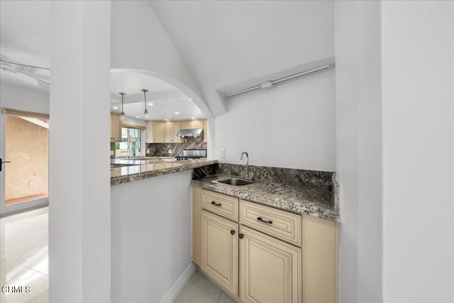 kitchen with light tile patterned floors, dark stone counters, decorative backsplash, sink, and lofted ceiling