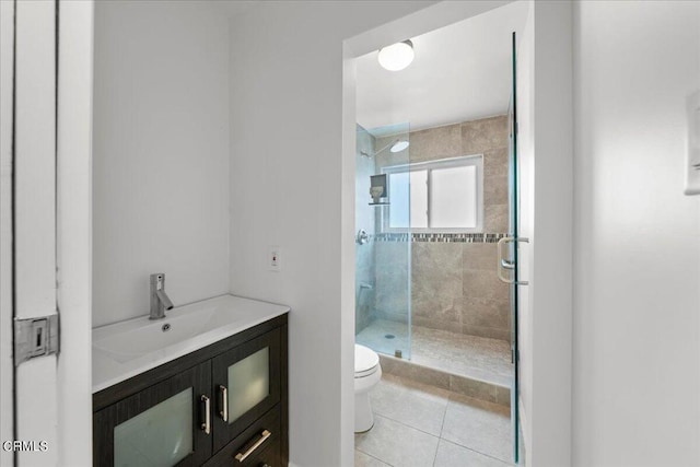 bathroom with toilet, tile patterned flooring, a tile shower, and vanity