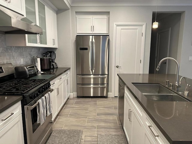 kitchen featuring stainless steel appliances, pendant lighting, sink, white cabinetry, and wall chimney range hood