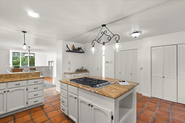 kitchen featuring white cabinetry, light stone counters, hanging light fixtures, a kitchen island, and stainless steel gas stovetop