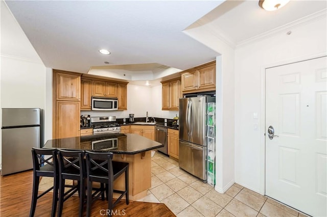 kitchen with appliances with stainless steel finishes, a breakfast bar, a kitchen island, a tray ceiling, and light tile patterned flooring